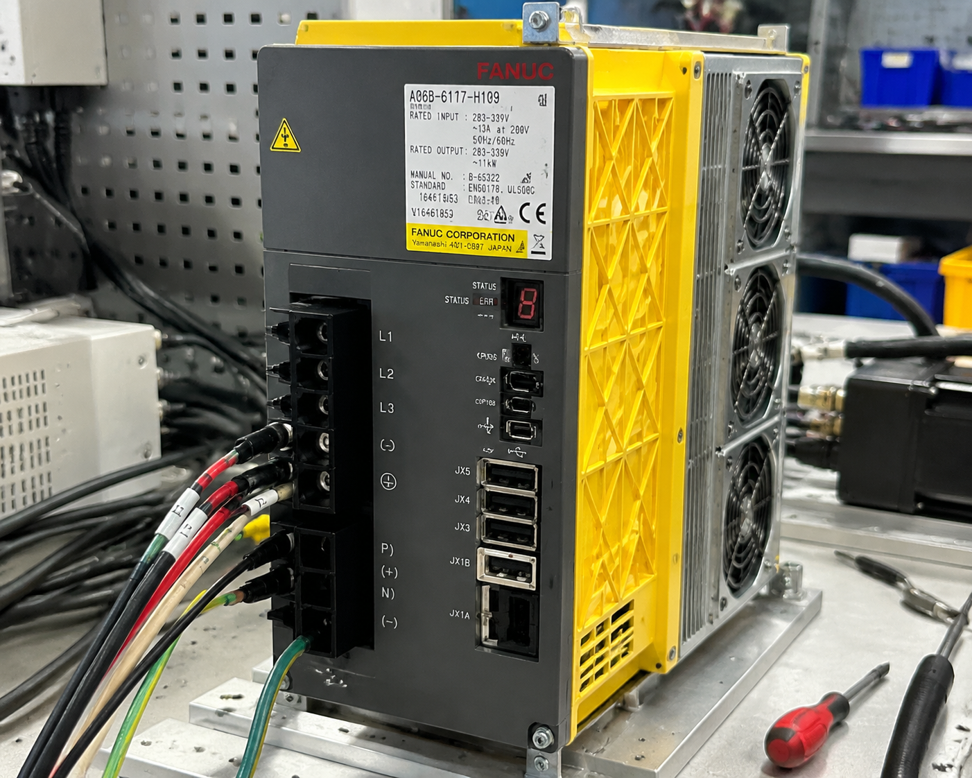 Close-up, high-resolution image of a FANUC A06B servo amplifier, clearly showing model number, power connectors, cooling fans, and control interface, mounted on a test bench, surrounded by tools and cables, clean industrial background, realistic lighting and reflections, detailed textures of metal and plastic, professional technical setting, precise and sharp focus, no text overlays